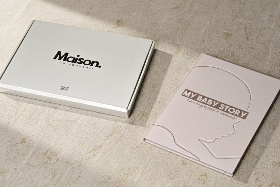 Livre de grossesse My Baby Story beige avec boîte Maison du Souvenir, photo sur fond clair, packaging élégant et minimaliste, cadeau naissance haut de gamme.
